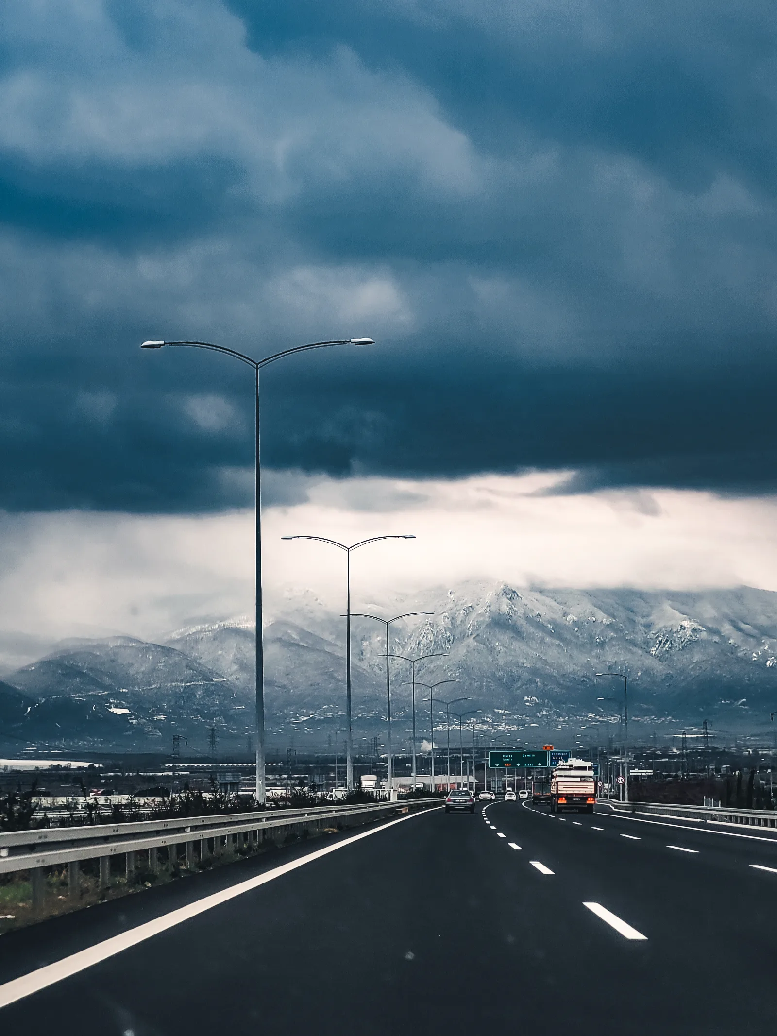 Highway running toward snow-capped mountains under storm cloud