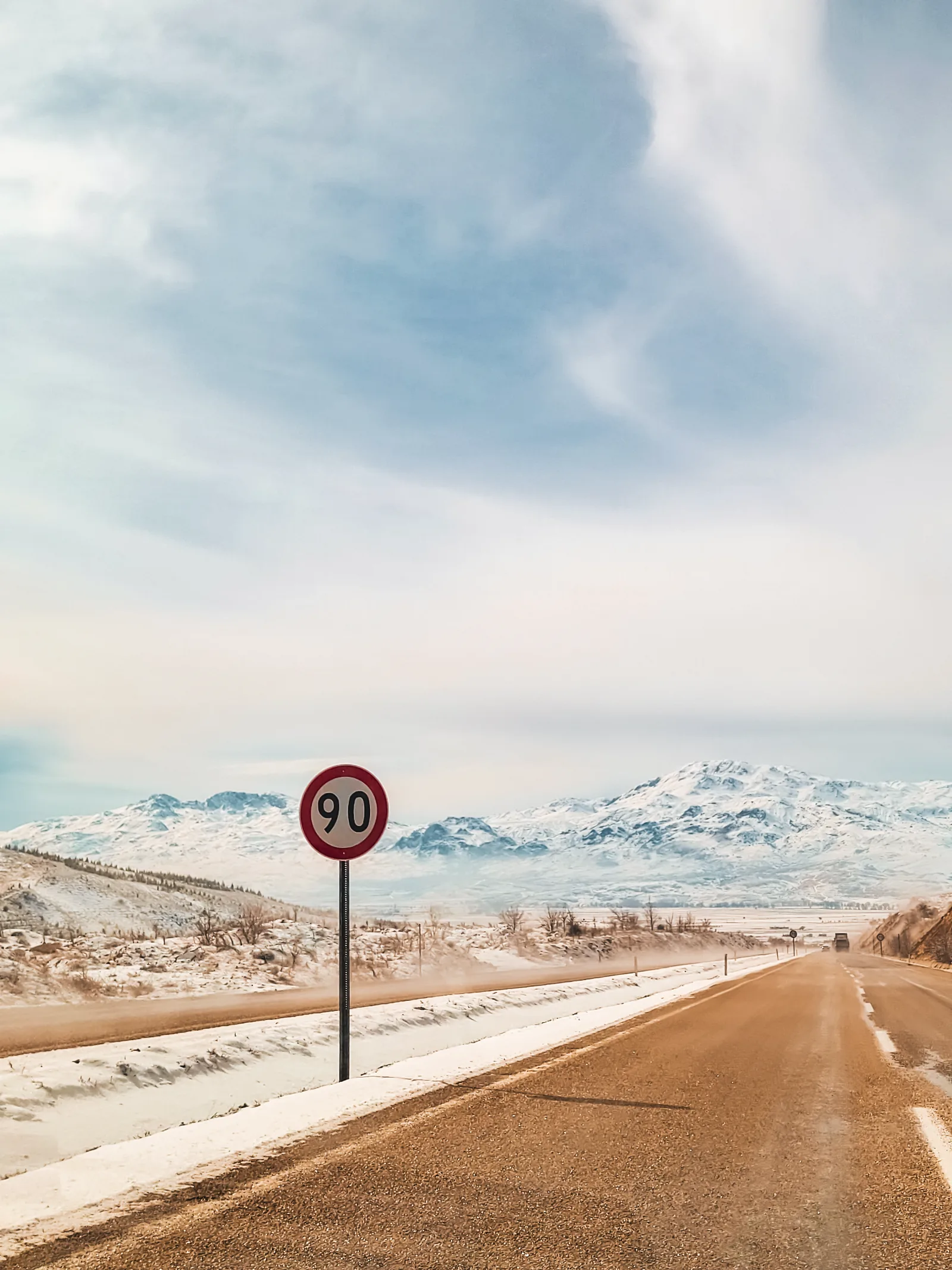 Speed limit sign on an empty road beside snowfields