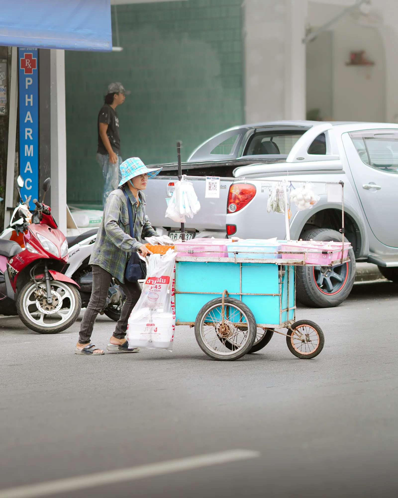 Vendor pushing a turquoise cart past a pharmacy