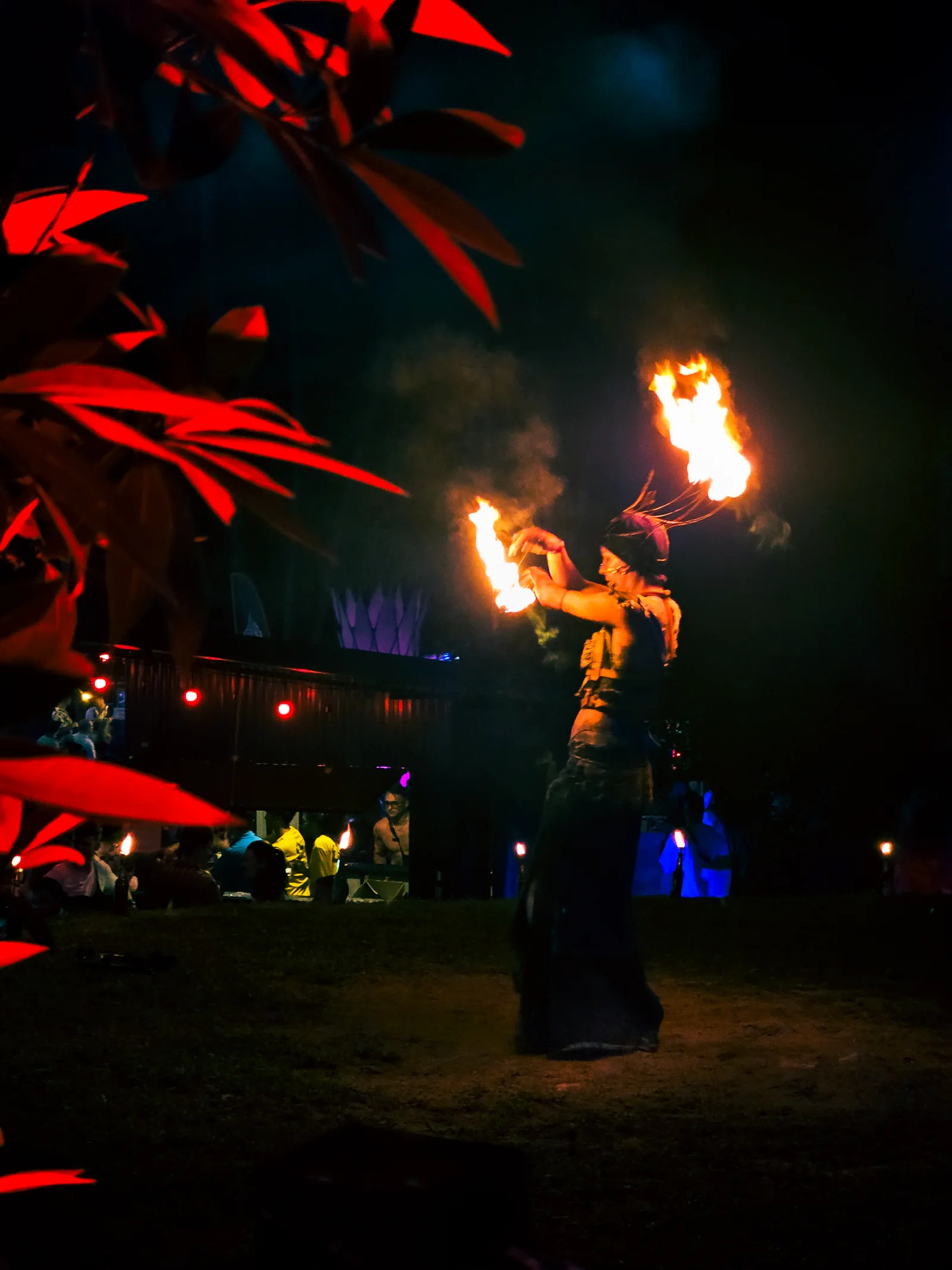Fire dancer performing under red-lit leaves